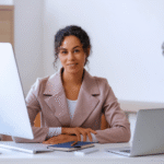 American businesswoman Jessica Miller in professional attire working on laptop at modern office desk, representing U.S. corporate environment and digital productivity