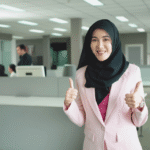 German executive Lena Weber in pink blazer giving double thumbs-up gesture in bright open-plan office, conveying confidence and success in German corporate culture
