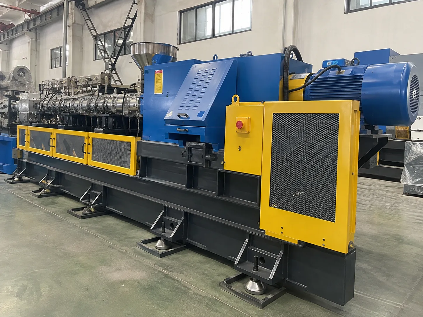 Heavy duty steel base frame with yellow safety guard and emergency stop on rubber extruder at UET